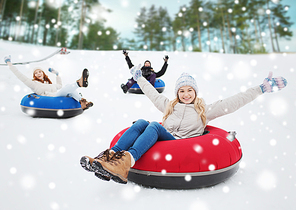 winter, leisure, sport, friendship and people concept - group of happy friends sliding down on snow tubes