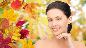 beauty, people, season and health concept - beautiful young woman touching her face over autumn leaves background