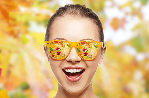 season, emotions and people concept - happy face of teenage girl in sunglasses with autumn leaves reflection over natural background