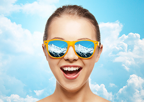 travel, tourism, winter, emotions and people concept - happy face of teenage girl in sunglasses with mountains reflection over blue sky and clouds background