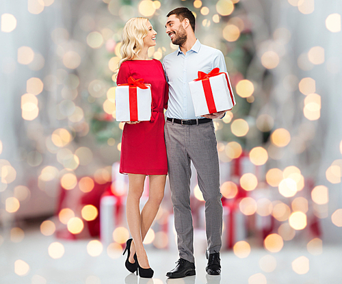 people, christmas, birthday, couple and holidays concept - happy young man and woman with gift boxes over christmas tree lights background