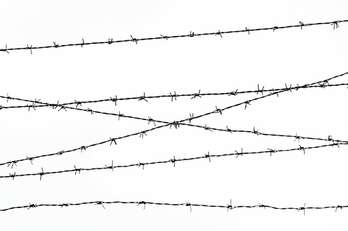 imprisonment, restriction concept - barb wire fence over gray sky