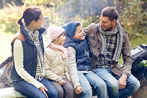 camping, travel, tourism, hike and people concept - happy family sitting on bench and talking at camp in woods