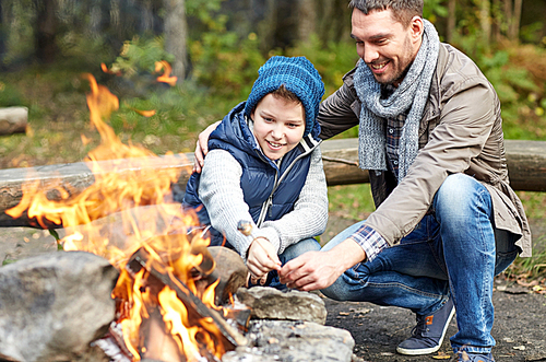 camping, tourism, hike, family and people concept - happy father and son roasting marshmallow over campfire
