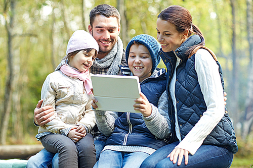 camping, tourism, hike, technology and people concept - happy family sitting on bench with with tablet pc computer at camp in woods