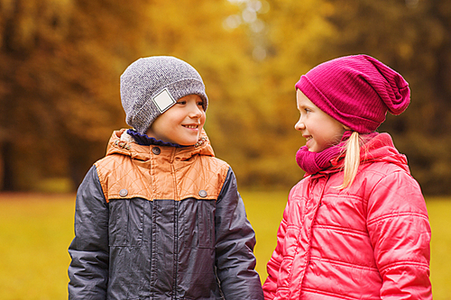 childhood, leisure, friendship and people concept - happy little girl and boy talking in autumn park