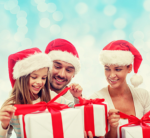 family, christmas, generation, holidays and people concept - happy family in santa helper hats with gift boxes over blue lights background