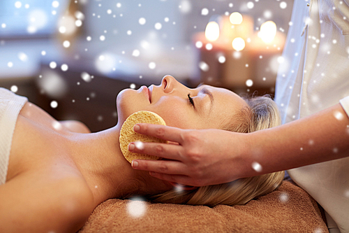 people, beauty, spa, skin care and relaxation concept - close up of beautiful young woman lying with closed eyes and having face massage with sponge in spa with snow effect