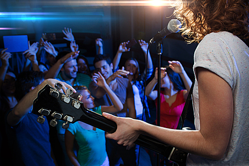 holidays, music, nightlife and people concept - close up of singer playing electric guitar and singing on stage over happy fans crowd waving hands at concert in night club