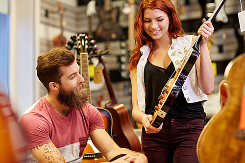 music, sale, people, musical instruments and entertainment concept - happy couple of musicians with electric guitar at music store