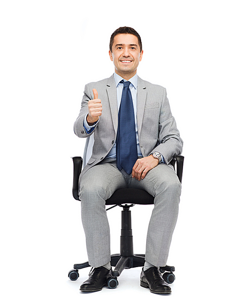 business, people, gesture and office concept - happy businessman in suit sitting in office chair and showing thumbs up