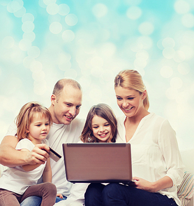 family, holidays, shopping, technology and people - happy family with laptop computer and credit card over blue lights background