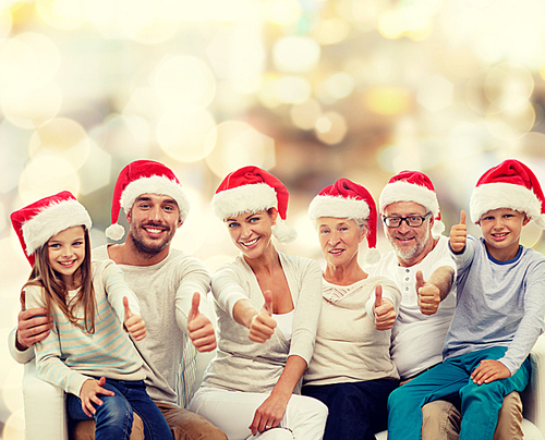 family, generation, gesture, holidays and people concept - happy family in santa helper hats showing thumbs up over lights background