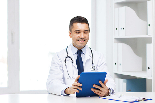 healthcare, profession, people and medicine concept - smiling male doctor in white coat with tablet pc in medical office