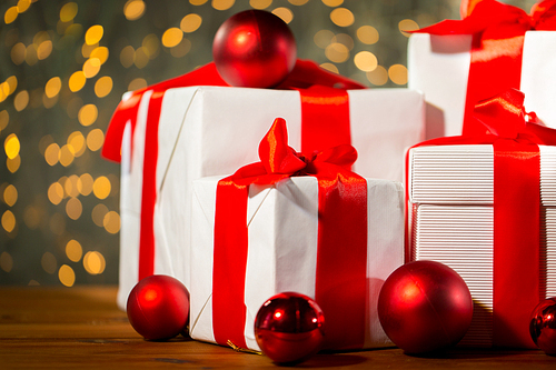 christmas, holidays, presents, new year and celebration concept - close up of gift boxes and red balls on wooden floor over lights background