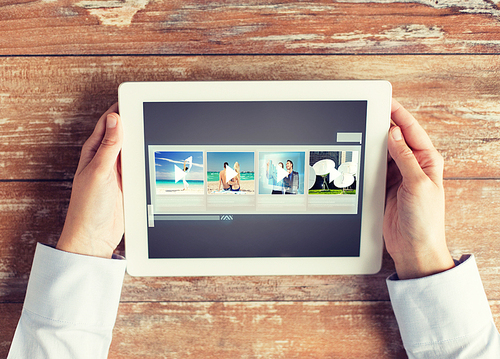 people, multimedia and technology concept - close up of hands with video gallery slideshow on tablet pc at table