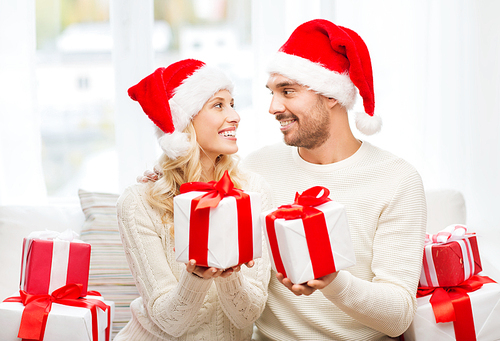 christmas, holidays and people concept - happy couple in santa hats exchanging gifts at home