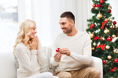 love, christmas, couple, proposal and people concept - happy man giving engagement ring in little red box to woman at home