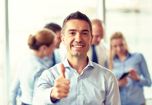 business, people, gesture and teamwork concept - smiling businessman showing thumbs up with group of businesspeople meeting in office