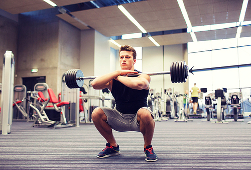 sport, bodybuilding, lifestyle and people concept - young man with barbell doing squats in gym