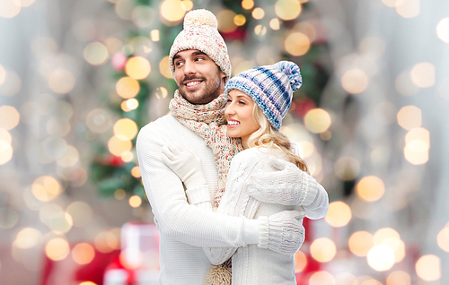 winter, fashion, couple, christmas and people concept - smiling man and woman in hats and scarf hugging over lights background