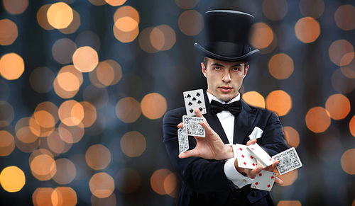 magic, gambling, casino, people and show concept - magician in top hat showing trick with playing cards over nigh lights background