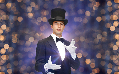 magic, performance, circus, people and show concept - magician in top hat showing trick over nigh lights background