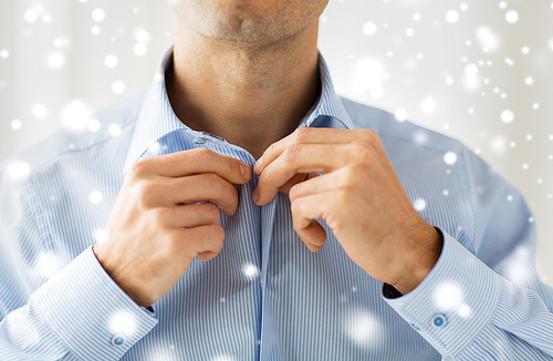 people, business, fashion and clothing concept - close up of man dressing up and fastening buttons on shirt at home over snow effect