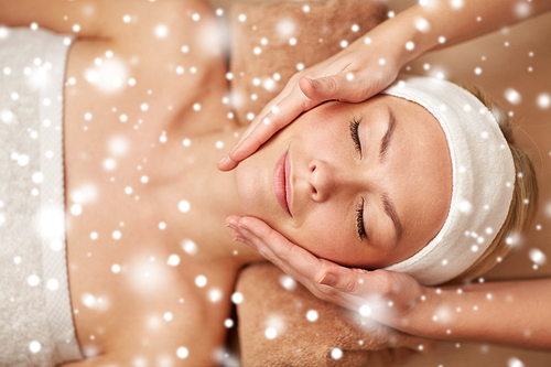 people, beauty, spa, winter and relaxation concept - close up of beautiful young woman lying with closed eyes and having face massage in spa with snow effect