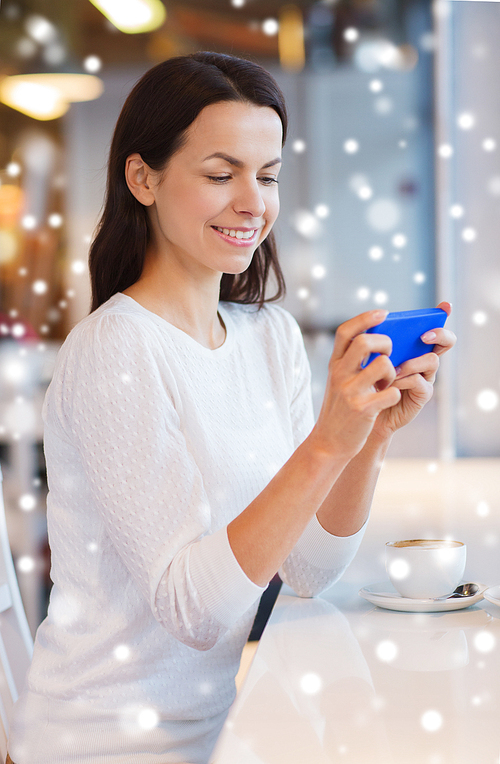 leisure, drinks, people, technology and lifestyle concept - smiling young woman with smartphone drinking coffee at cafe with snow effect