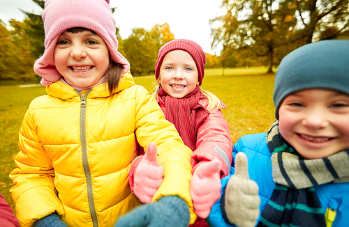 childhood, leisure, friendship and people concept - group of happy kids showing thumbs up in autumn park