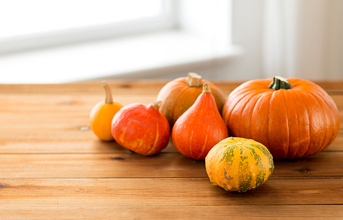 food, harvest, season and autumn concept - close up of pumpkins on wooden table at home