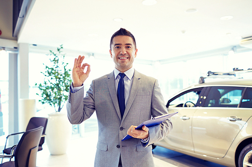 auto business, car sale, consumerism, gesture and people concept - happy man with clipboard showing thumbs up at auto show or salon