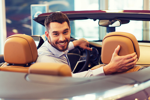 auto business, car sale, consumerism and people concept - happy man sitting in car at auto show or salon