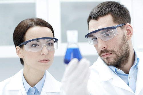 science, chemistry, research, biology and people concept - young scientists holding flask with medicine or chemical in clinical laboratory