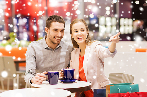 sale, shopping, consumerism, leisure and people concept - happy couple with shopping bags drinking coffee in mall with snow effect