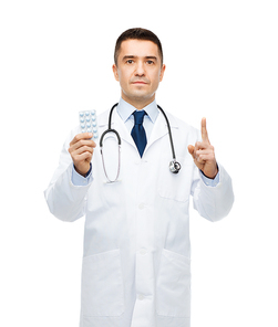 healthcare, profession, people and medicine concept - male doctor in white coat with tablets pointing his finger up