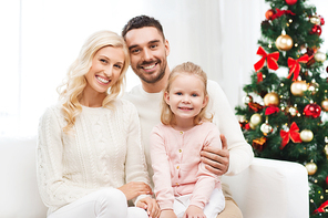 family, christmas, holidays and people concept - happy mother, father and little daughter sitting on sofa at home