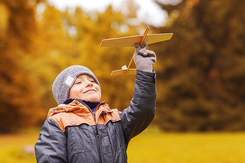 autumn, childhood, dream, leisure and people concept - happy little boy playing with wooden toy plane outdoors