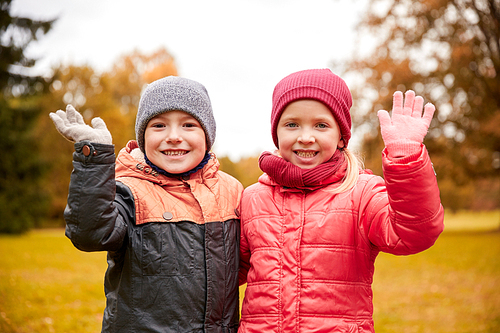 childhood, leisure, friendship, autumn and people concept - happy little girl and boy waving hands in park