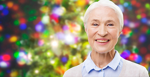 holidays, age and people concept - happy smiling senior woman face over christmas holidays lights background