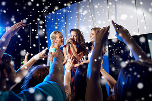 party, holidays, celebration, nightlife and people concept - happy young women singing karaoke on night club stage and snow effect