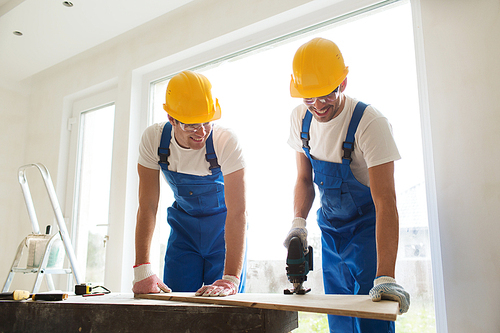 business, building, teamwork and people concept - group of smiling builders in hardhats with tools indoors