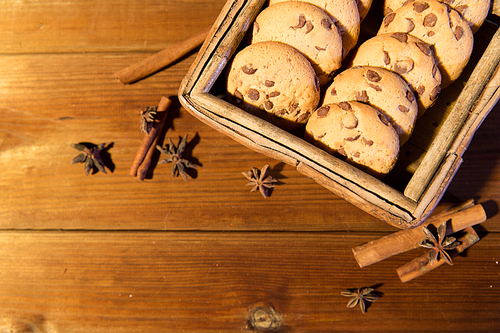 baking, culinary, holidays and food concept - close up of oat cookies in wooden box, and cinnamon on table