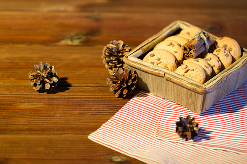 christmas, baking, culinary, holidays and food concept - close up of oat cookies in wooden box with cinnamon and pinecones on table