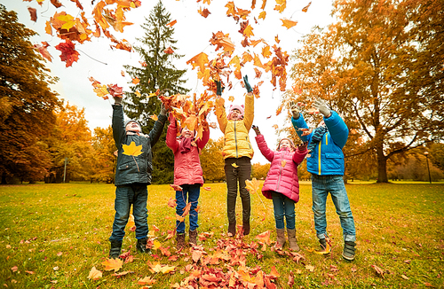 childhood, leisure, friendship and people concept - group of happy kids playing with autumn maple leaves and having fun in park