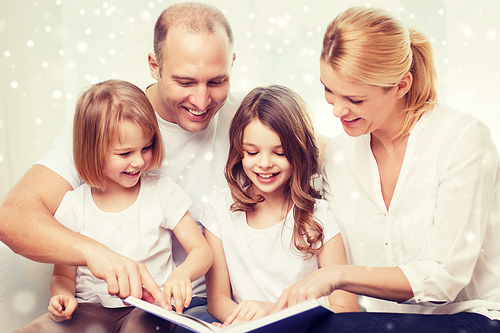 family, leisure, education and people - smiling mother, father and little girls reading book over snowflakes background