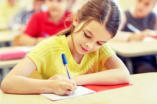 education, elementary school, learning and people concept - group of school kids with pens and notebooks writing test in classroom