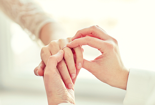 people, homosexuality, same-sex marriage and love concept - close up of happy lesbian couple hands putting on wedding ring