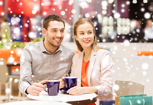 sale, shopping, consumerism, leisure and people concept - happy couple with shopping bags drinking coffee in mall with snow effect